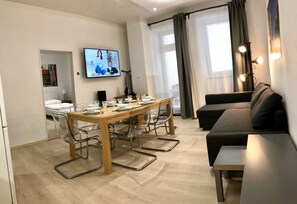 Una sala de estar moderna con comedor, televisor montado en la pared y un sofá.