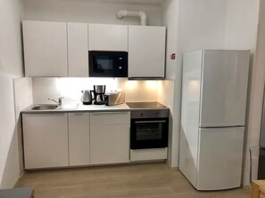 A compact kitchen with white cabinetry, a microwave, a toaster, a kettle, and a refrigerator. - Spacious 1-bedroom apartment in Prague Old Town (Prague)