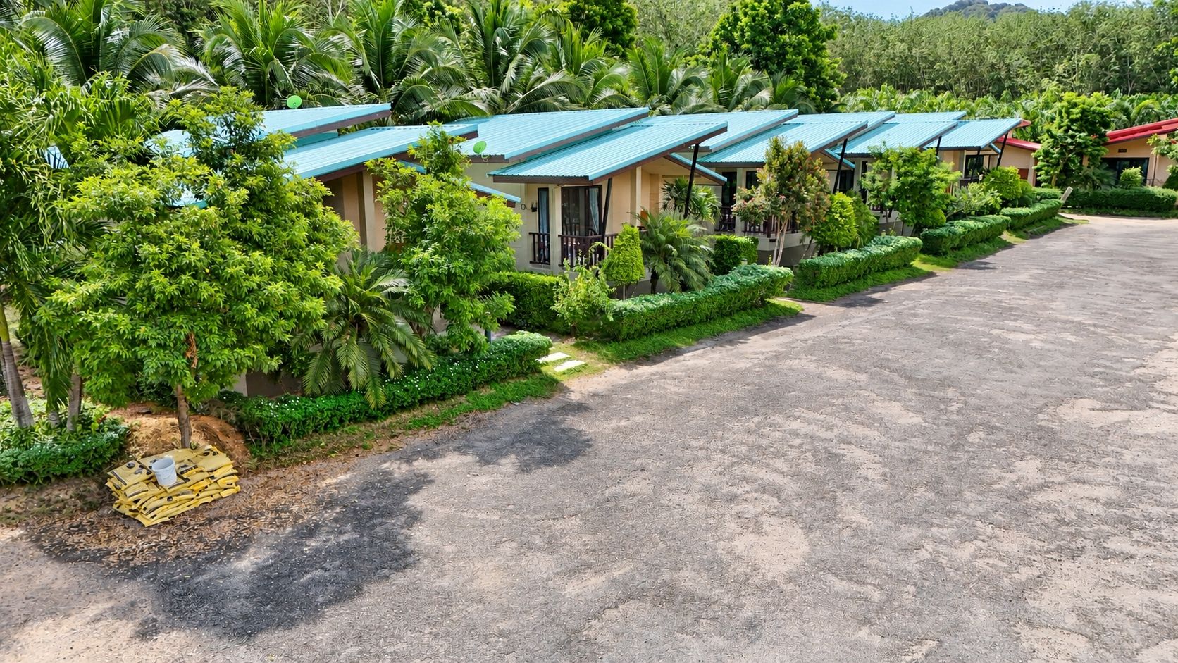 A row of single-story buildings with blue roofs, surrounded by lush greenery and a paved driveway.