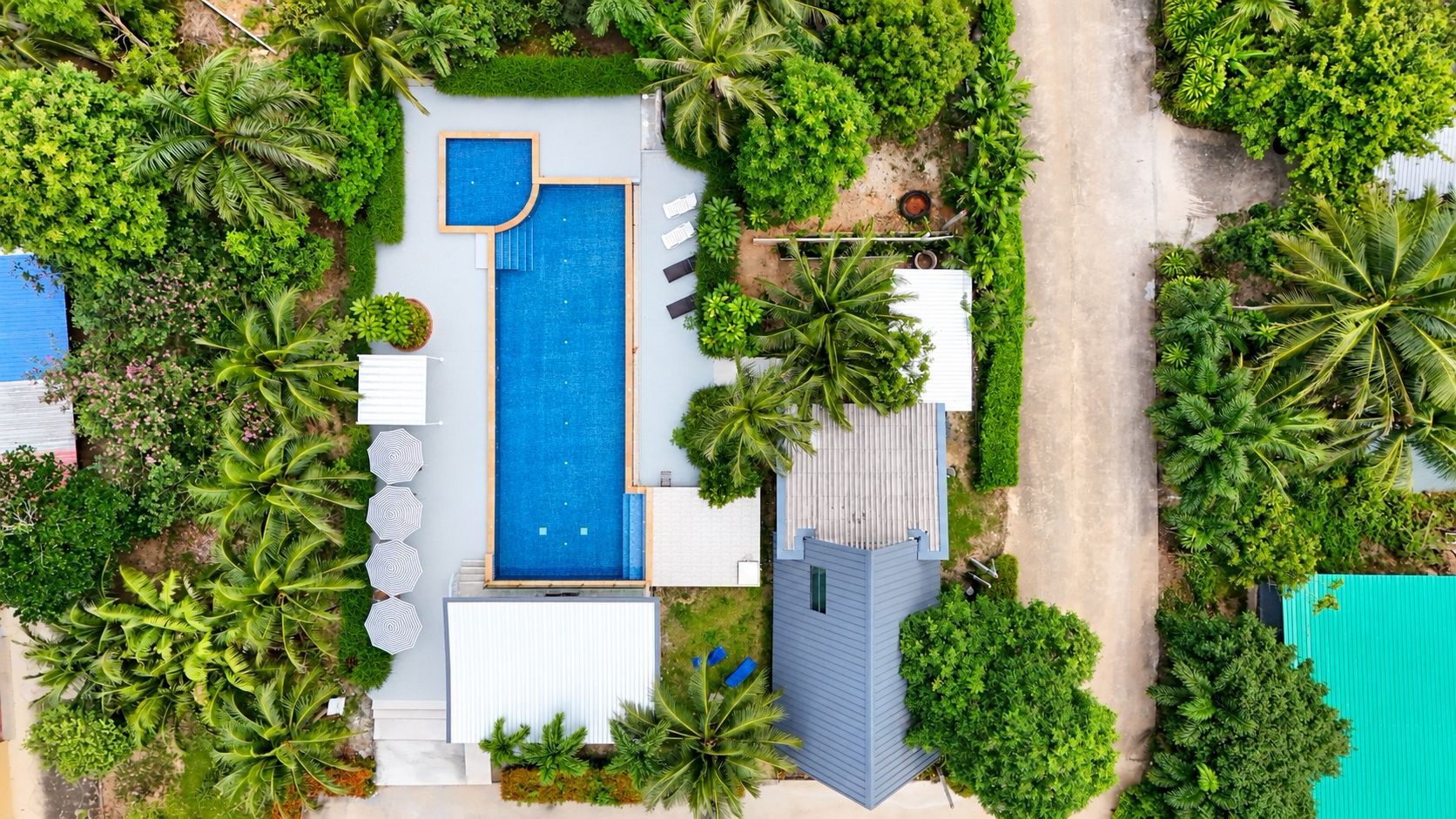 An aerial view of a property with a swimming pool, surrounded by lush greenery and palm trees.