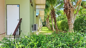 A corridor with a door, air conditioning units, and a pathway lined with palm trees and greenery. - Flow Krabi resort (Krabi)