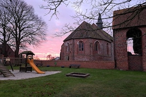 Ein Spielplatz mit einer Rutsche und einem Backsteinhaus mit Rundbogenfenstern.