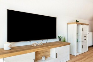 A modern living room with a large flat-screen TV mounted on the wall, a wooden coffee table, and a white cabinet with drawers. - Freddy's Beach House (Cuxhaven)