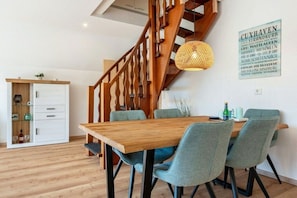 A dining area with a wooden table and chairs, a staircase, and a wall-mounted sign. - Freddy's Beach House (Cuxhaven)