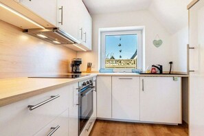 Eine kompakte Küche mit weißen Schränken, einem eingebauten Backofen und einem Fenster mit Blick auf einen Balkon.