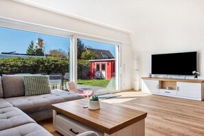 A modern living room with a sofa, a coffee table, and a TV on a wooden cabinet. - Freddy's Beach House (Cuxhaven)