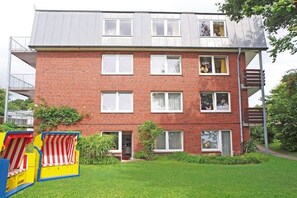 Un edificio de varios pisos de ladrillo con techo plano, múltiples ventanas y un pequeño jardín delantero.