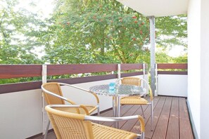 A balcony with wicker chairs and a glass table, surrounded by a wooden deck and a white wall. - in the Wattenlöper apartment building (Cuxhaven)