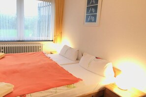 A hotel room with a bed, a radiator, a window with curtains, and a wall-mounted picture. - in the Wattenlöper apartment building (Cuxhaven)