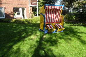 A small, colorful play structure with a striped canopy, situated in a grassy area with a brick building in the background. - in the Wattenlöper apartment building (Cuxhaven)