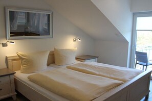A bedroom with two beds, a nightstand, a lamp, and a painting on the wall. - At the canal footbridge (Krummhörn-Greetsiel)