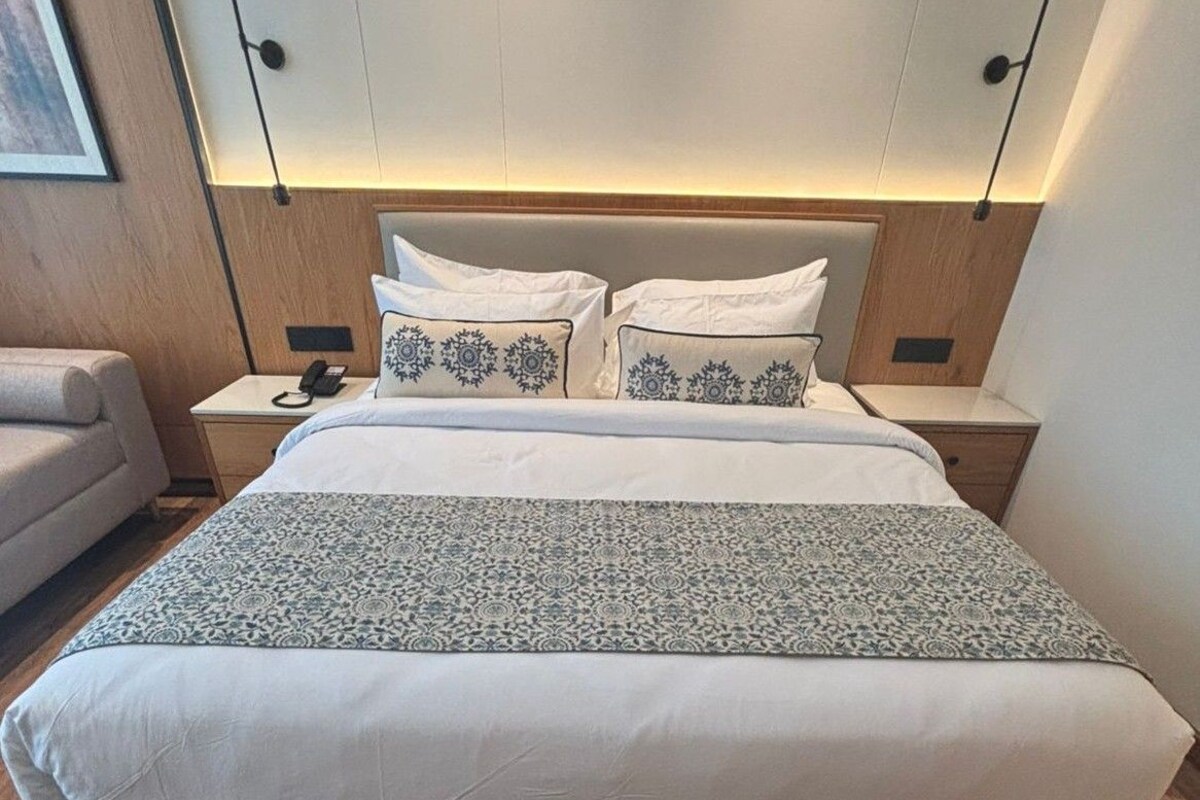 Een hotelkamer met een groot bed, een nachtkastje met een lamp, een stoel en een aan de muur bevestigde televisie.