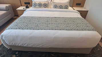 A hotel room with a large bed, a bedside table with a lamp, a chair, and a wall-mounted TV.