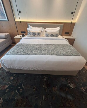 Een hotelkamer met een groot bed, een nachtkastje met een lamp, een stoel en een aan de muur bevestigde televisie.