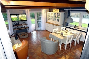 A dining area with a table set for four, a cabinet with glass doors, and a television mounted on the wall. - Holiday home in Hooksiel with swimming pool (Hooksiel)