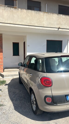 A beige car parked in front of a building with a white facade, a small window, and a door. - Holiday Home 'Angel’s House' (San Giovanni Suergiu)