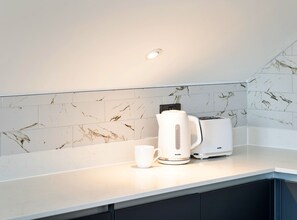 Una cocina con baldosas de mármol blanco, una cafetera Breville, un tostador y una taza blanca sobre la encimera.