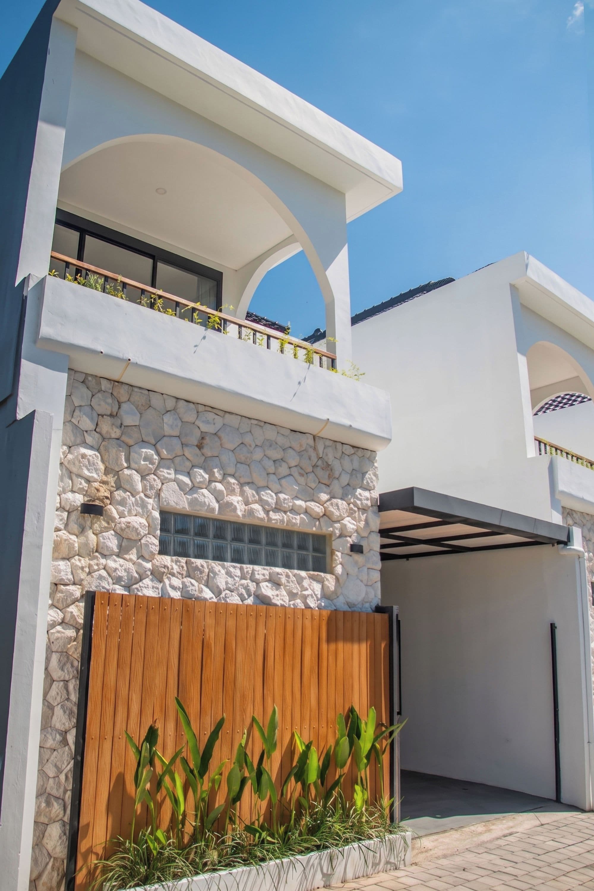Una casa moderna de dos pisos con fachada de piedra, cerca de madera y un garaje.