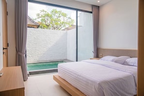 Un dormitorio con cama, mesita de noche, ventana y vista a una piscina.