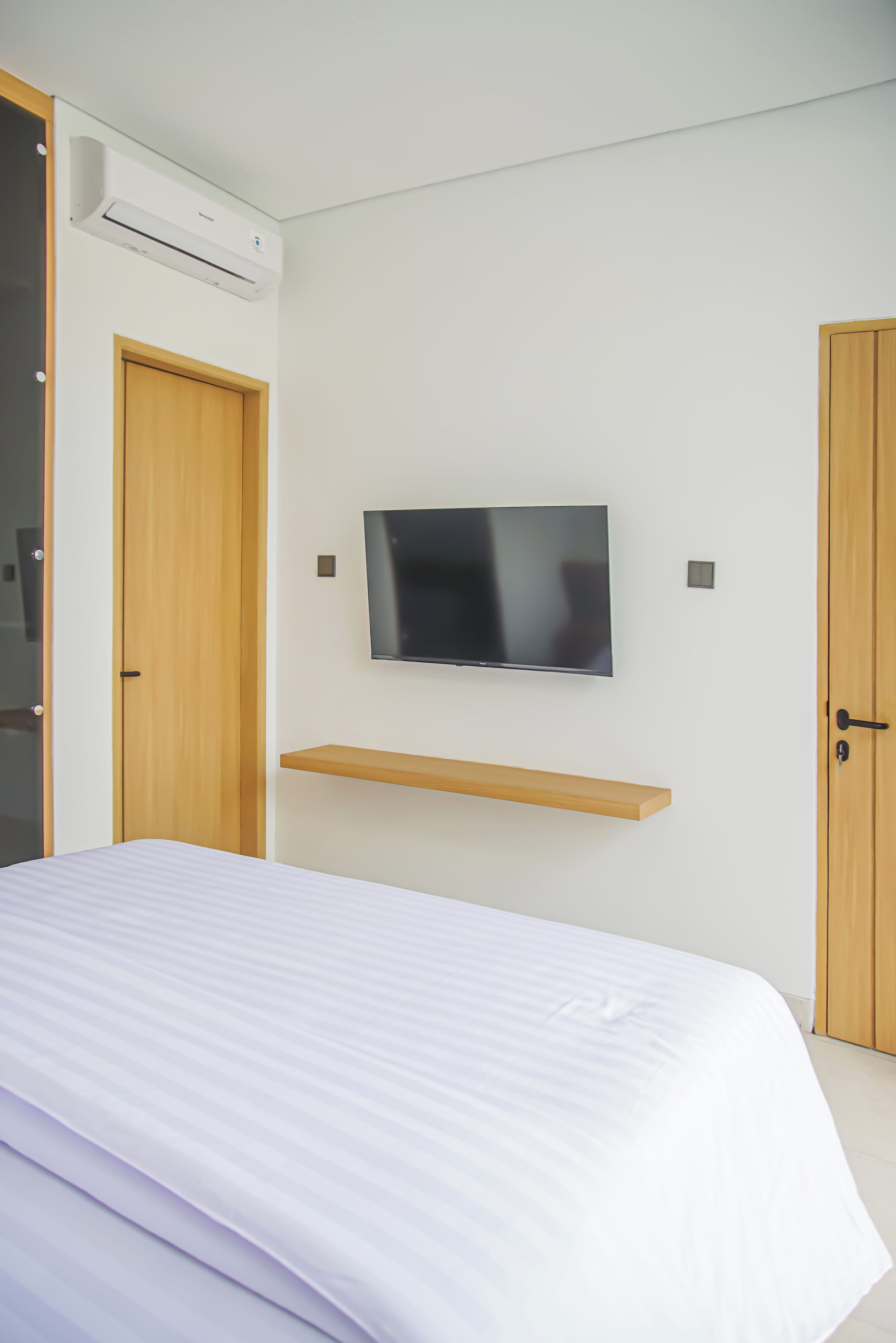 Un dormitorio con una cama, un televisor montado y dos puertas.