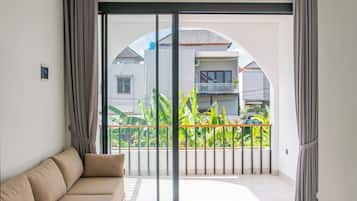 Un salón moderno con sofá, puertas correderas de cristal que dan a un balcón con vistas a casas vecinas y zonas verdes.