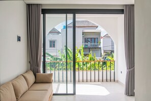 Un salón moderno con sofá, puertas correderas de cristal que dan a un balcón con vistas a casas vecinas y zonas verdes.