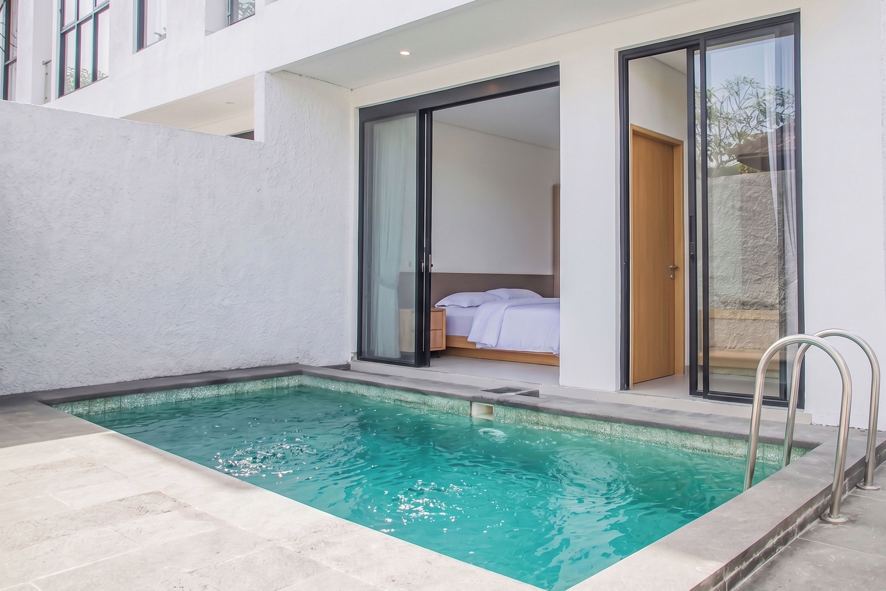 A modern hotel room with a private pool, large sliding glass doors, and a visible bed.