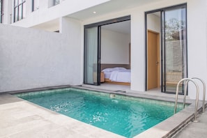 Una habitación de hotel moderna con piscina privada, puertas correderas de vidrio grandes y una cama visible.