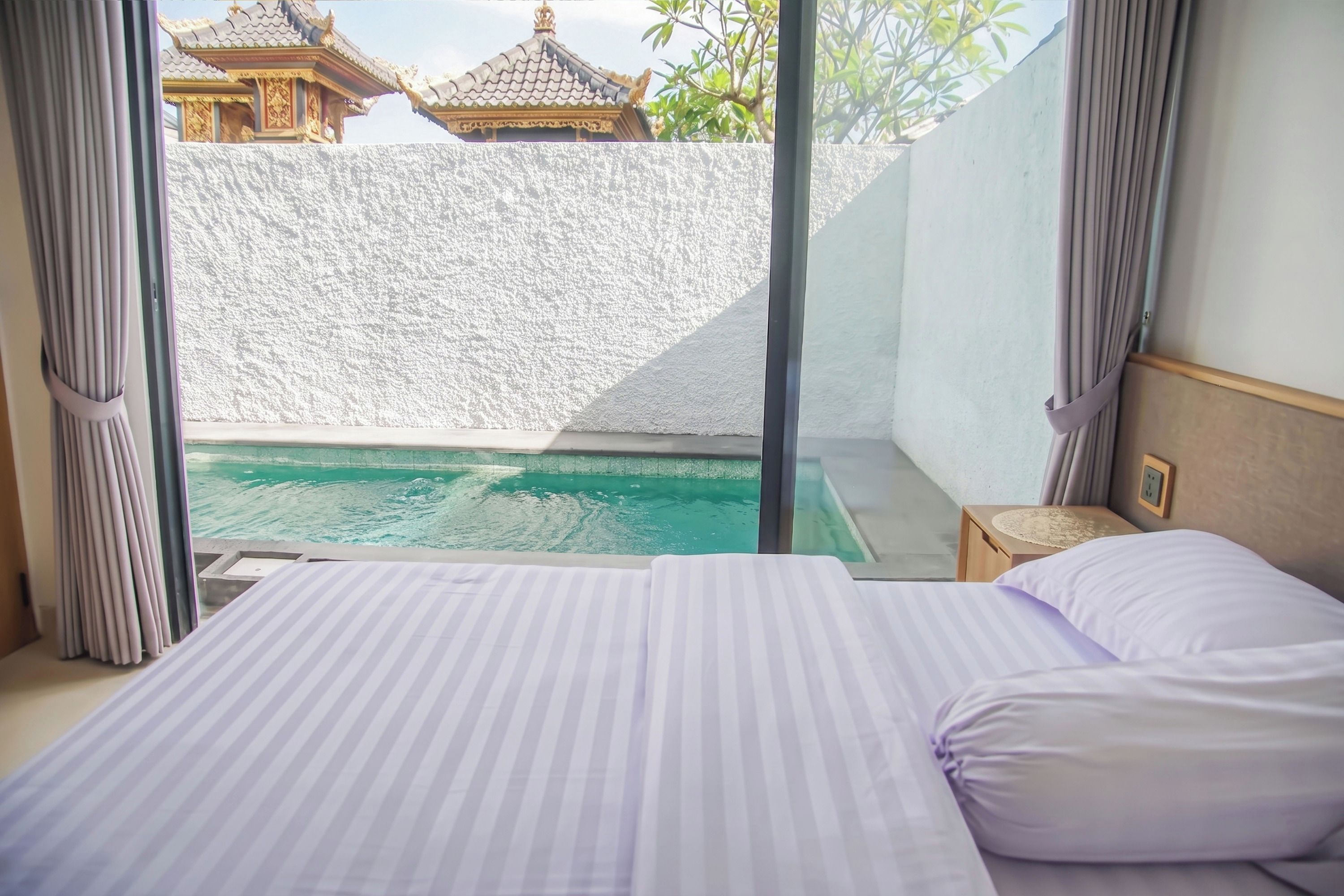 Una habitación de hotel con una cama, vista a una piscina y un edificio tradicional al fondo.