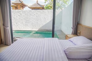 A hotel room with a bed, a view of a swimming pool, and a traditional building in the background. - Saura Villas (Buduk)