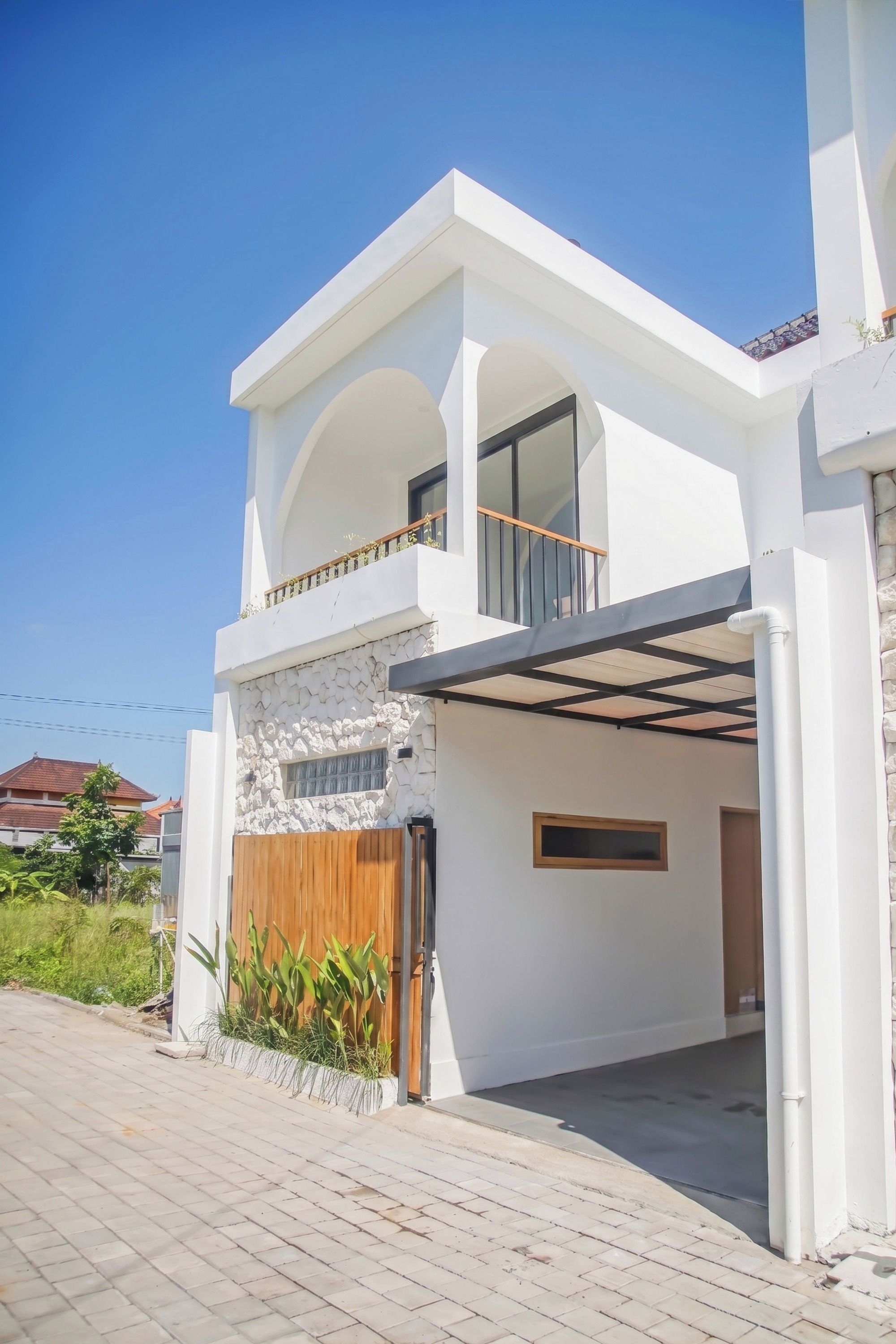 A modern two-story house with a stone facade, a wooden gate, and a balcony.