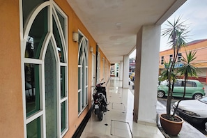 A covered walkway with a motorcycle parked, potted plants, and a green car parked outside. - Hotel Sahara Rawang (Rawang)
