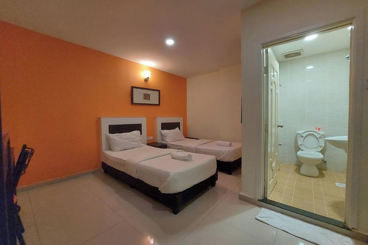 A hotel room with two beds, a bathroom with a toilet and sink, and a glass door leading to the bathroom.