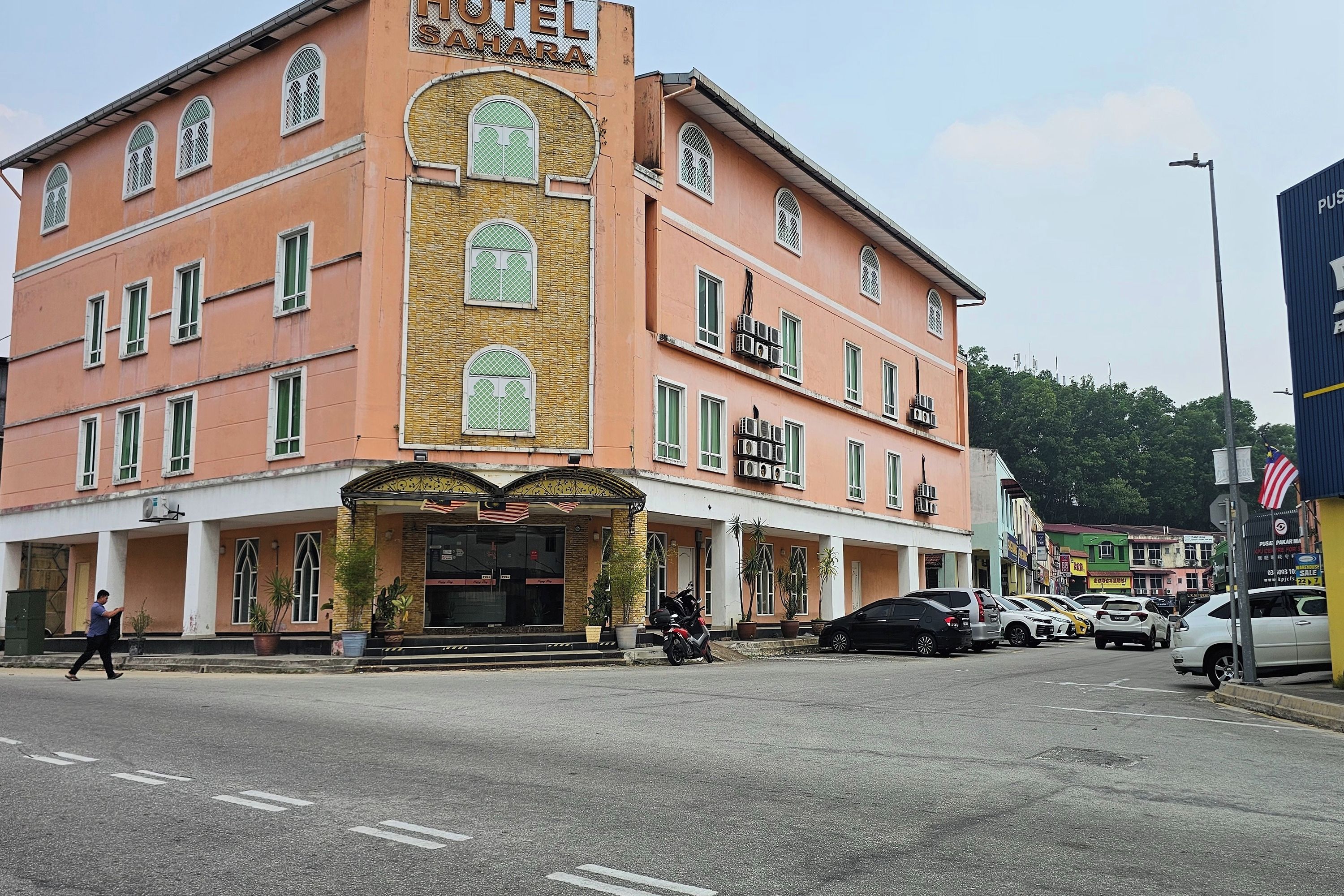 Un hotel con un letrero llamativo, varias ventanas y vista a la calle con coches estacionados.