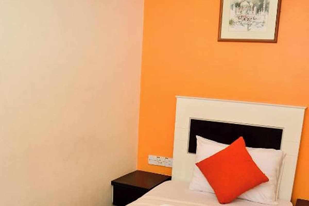 A single bed with a white and red bedspread, a black headboard, and a red pillow. There is a white wall with a framed picture above the bed.