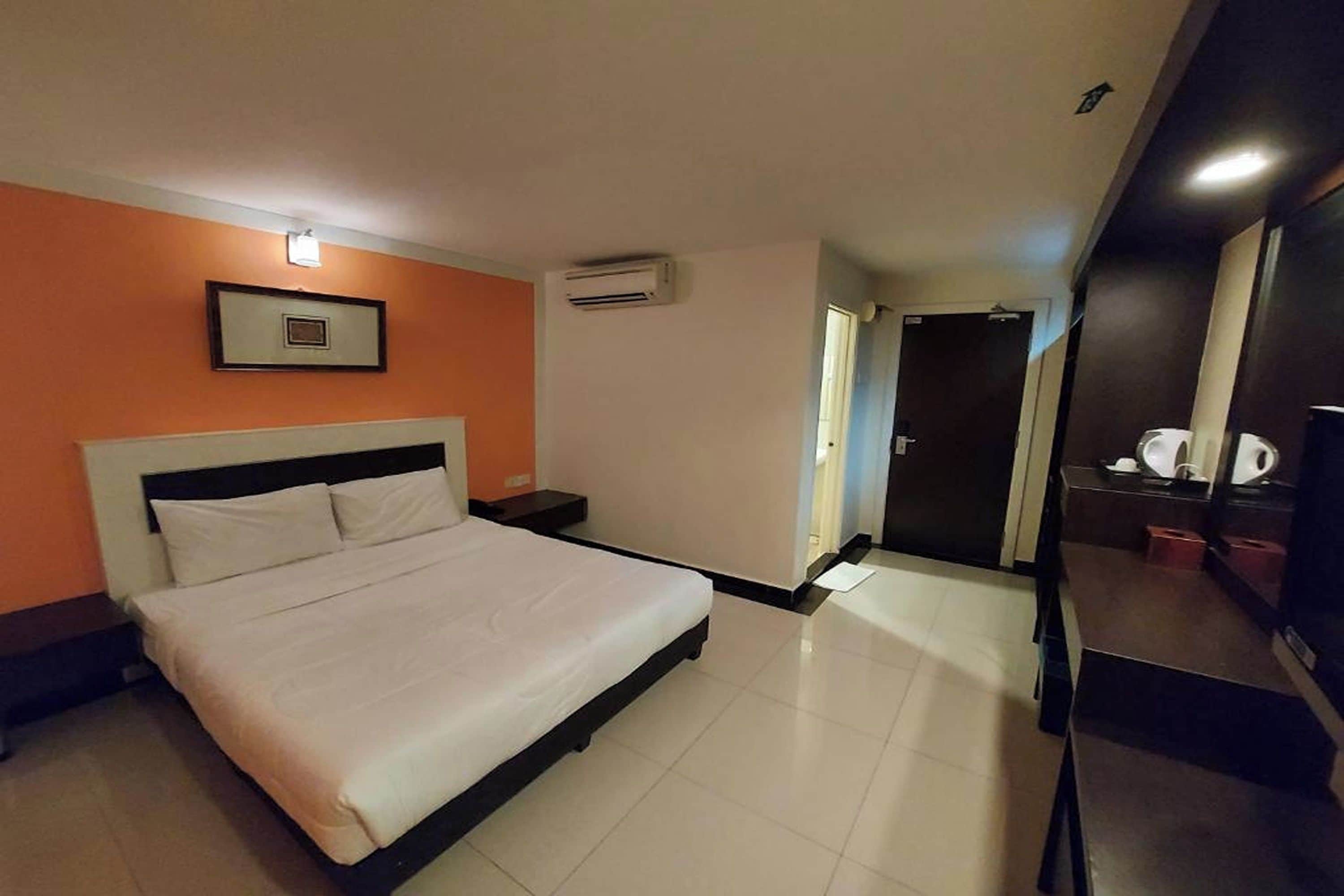 A hotel room with a bed, nightstands, an air conditioning unit, a mirror, and a door leading to a bathroom.