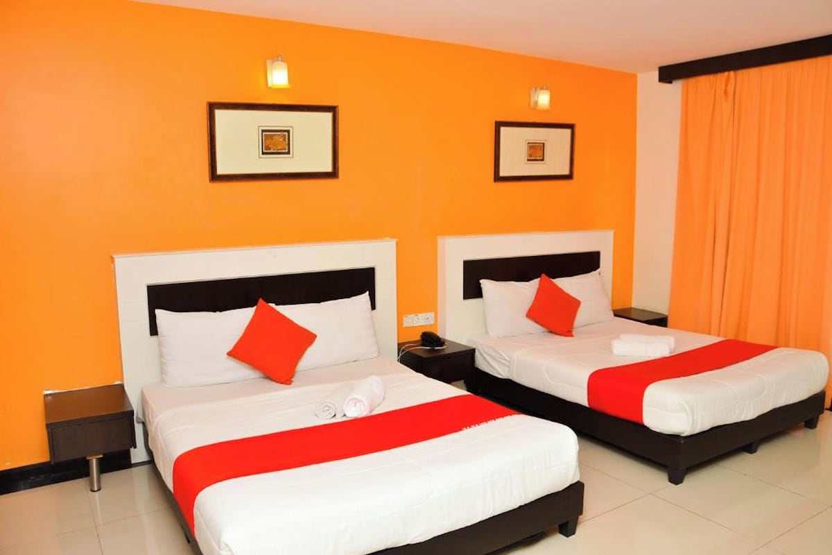 A hotel room with two beds, each with white bedding and red accents, and orange walls.