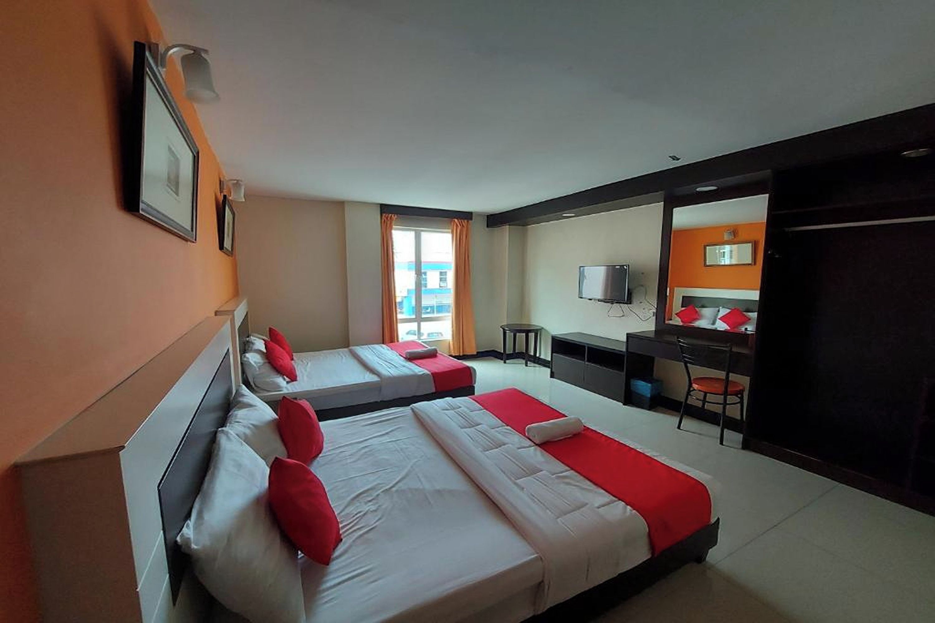 Una habitación de hotel con dos camas, un escritorio, una silla, un televisor y una ventana con cortinas.