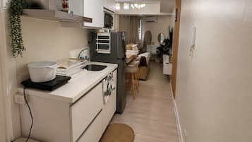 Cocina compacta con un lavamanos, un microondas y un refrigerador pequeño. Hay un comedor con una silla y una mesa.