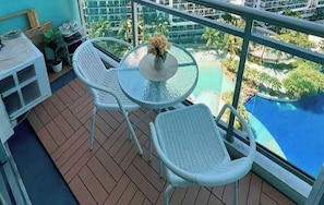 A balcony with a round table and two chairs, overlooking a swimming pool and greenery. - Azure Urban Resort Residences Parañaque (Paranaque)