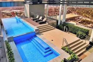 Piscina no terraço com vista para a cidade, escadas descendo até a piscina e espreguiçadeiras.