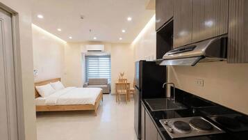 A compact hotel room with a bed, kitchenette, and a small dining area.
