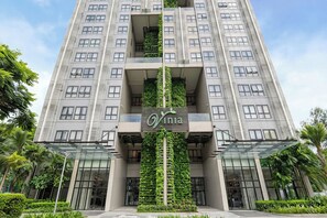 Um edifício alto com design moderno, apresentando um jardim vertical central e um logotipo na fachada.
