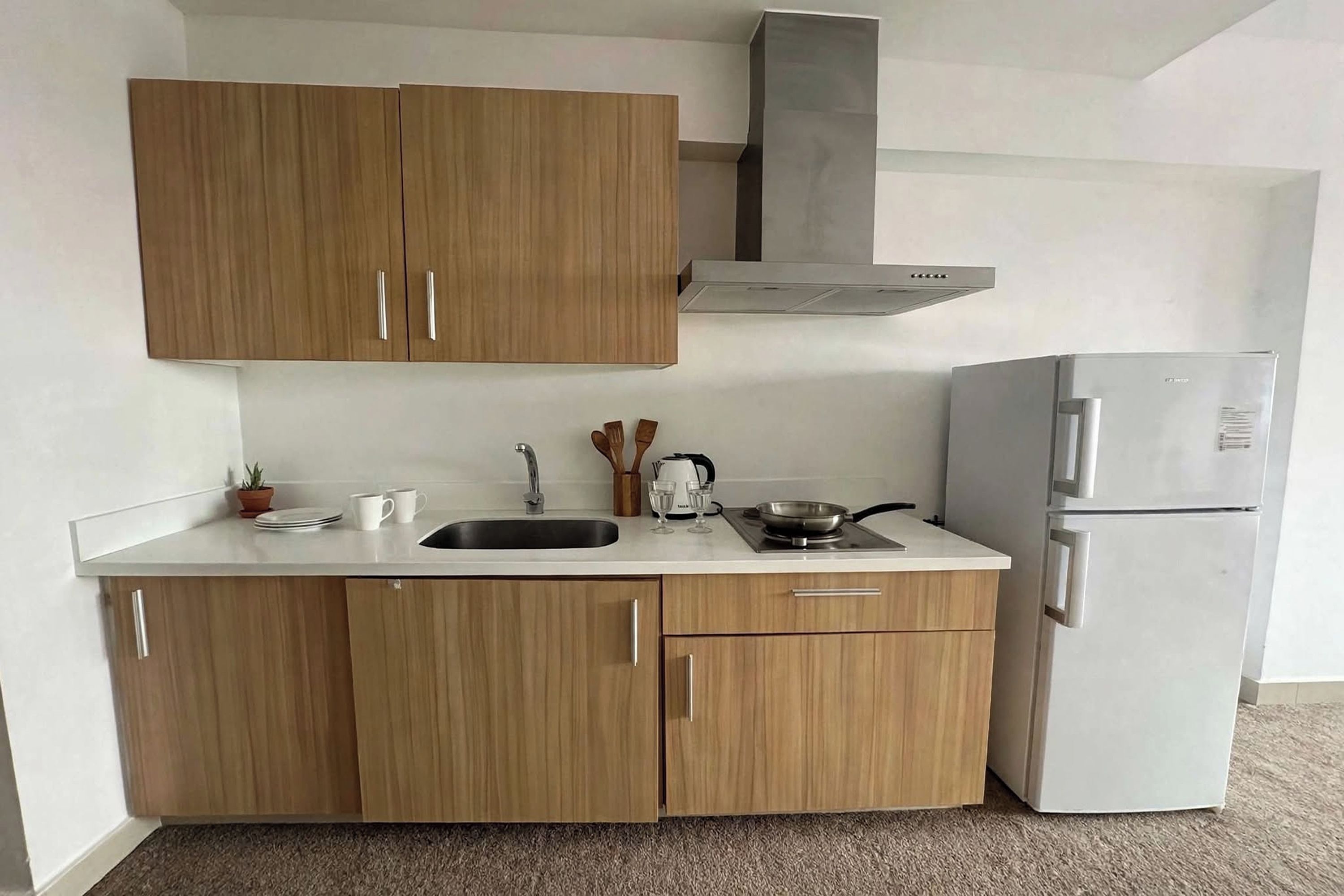A compact kitchen with wooden cabinets, a stainless steel refrigerator, and a gas stove.