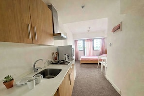 Cocina compacta con lavamanos, estufa y armarios, que da paso a un dormitorio con cama y ventana.