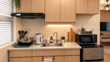 A modern kitchen with wooden cabinets, a stainless steel sink, a kettle, a toaster, a microwave, and a refrigerator.