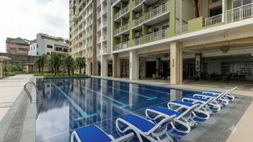 A swimming pool with lounge chairs, a multi-story building with balconies, and palm trees.