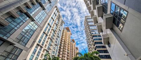 Un edificio de gran altura con varios balcones y amplias ventanas, rodeado de palmeras.
