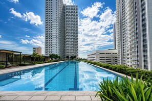 Una piscina con un cielo azul despejado y altos edificios residenciales al fondo.