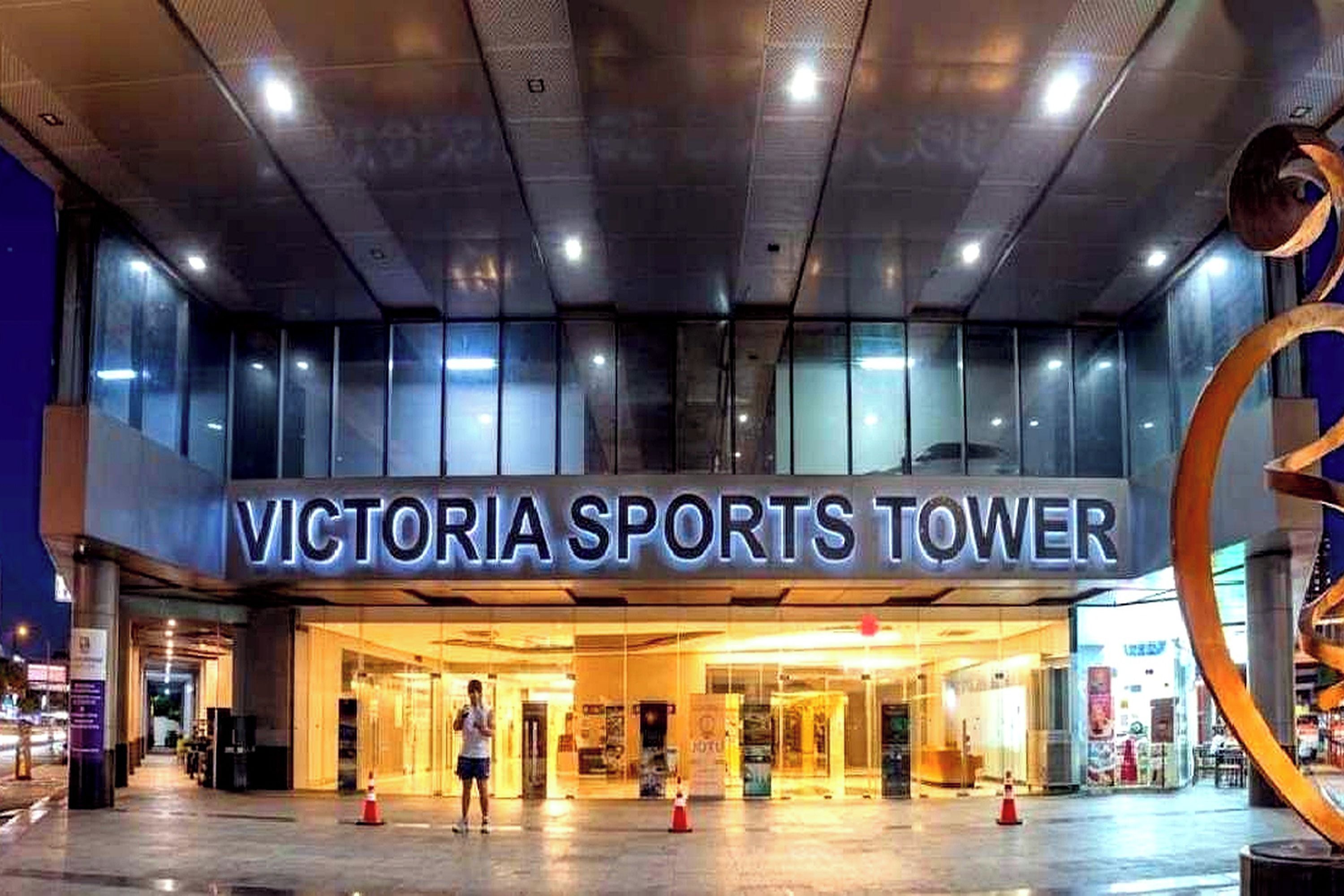 The exterior of Victoria Sports Tower with a prominent entrance and a large glass facade.